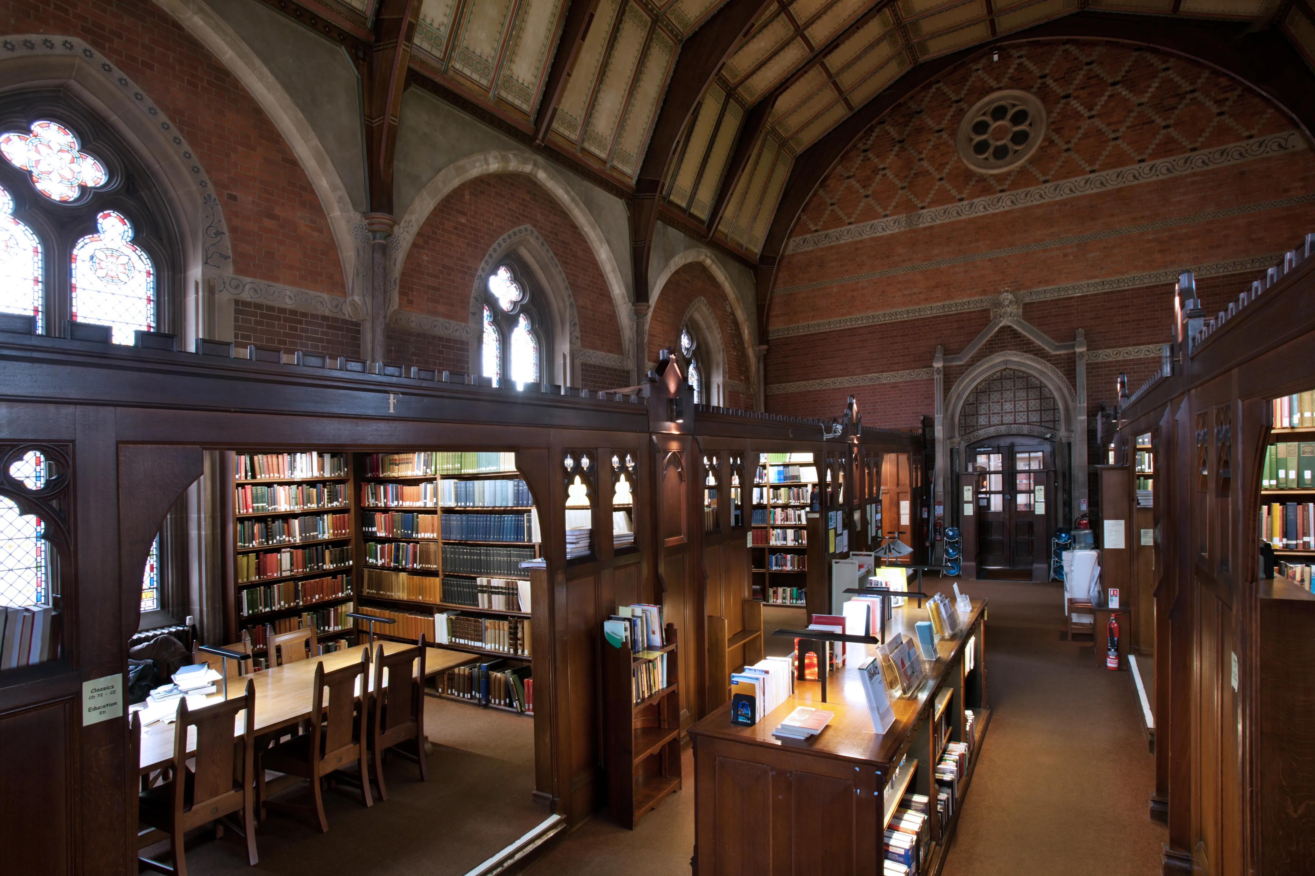 Gewelfd bibliotheekinterieur met veelkleurige bakstenen bogen, houten boekenplanken, leestafels en gotische boogramen in Keble College