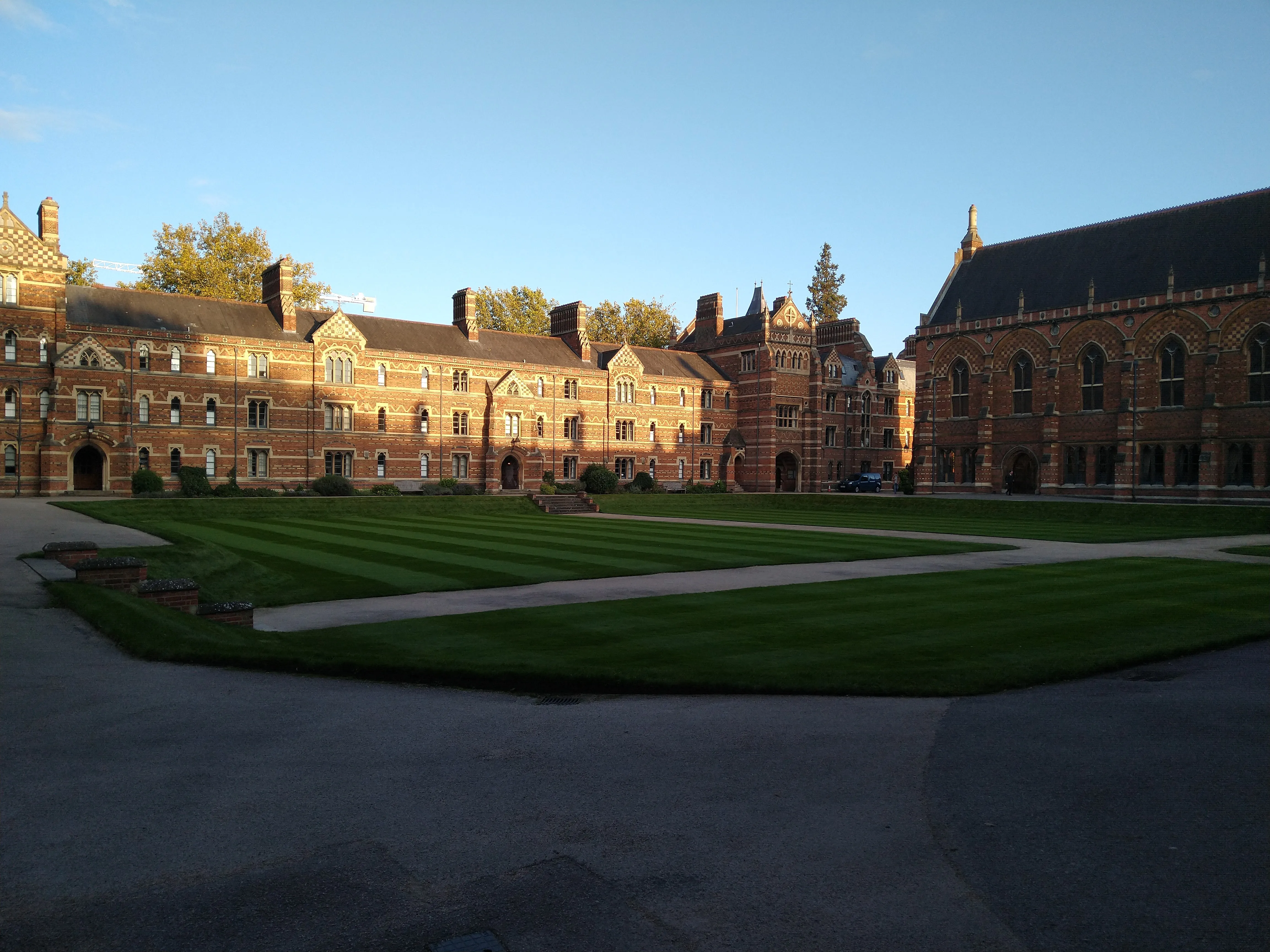 Wijdse blik op Liddon Quad van Keble College met rood- en geelgekleurde bakstenen gebouwen in victoriaanse gotische stijl rondom een strak gazon onder een helderblauwe lucht.