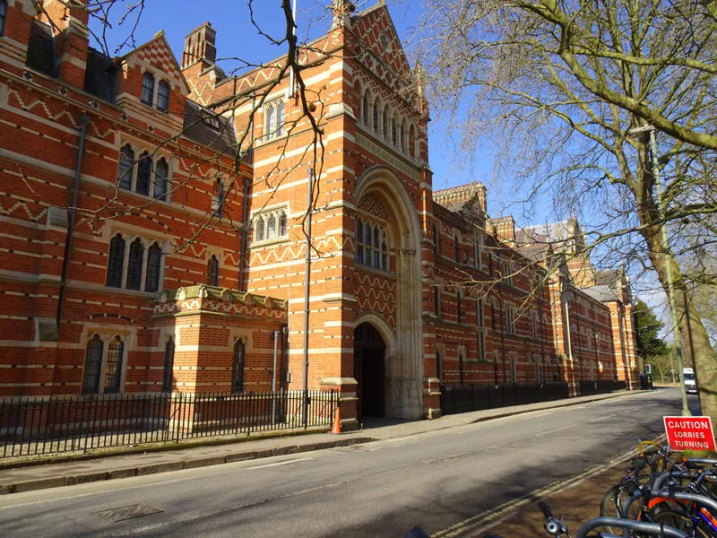 Victoriaans-gotische gevel van rode baksteen van Keble College met opvallend polychroom metselwerk en stenen banden, gezien vanaf de straat met fietsen die in de buurt geparkeerd staan.