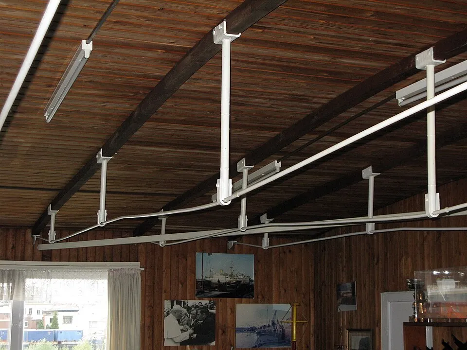 Techo de madera con sistema de rieles de tubería blanca y lámparas fluorescentes dentro de una habitación con fotografías históricas exhibidas en paredes revestidas de madera
