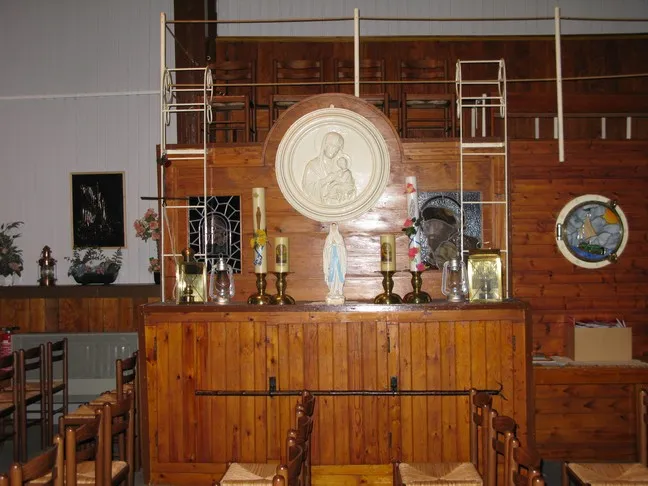 Altar de madera dentro del Kerkschip Sint-Jozef que presenta velas, una estatua de la Virgen María y un gran relieve religioso circular.