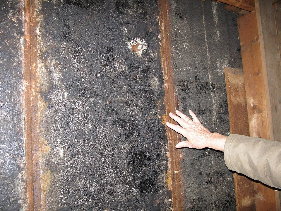 Primer plano de vigas de metal oxidadas y la superficie oscura y texturizada del casco con una mano tocando la estructura