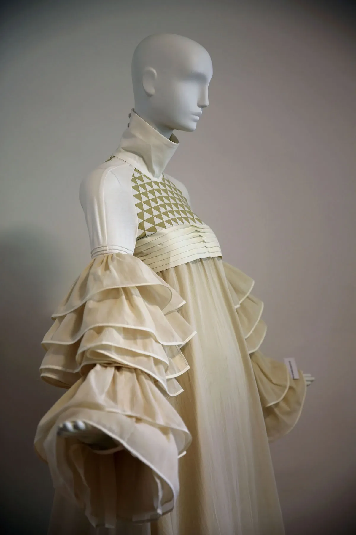 A mannequin wearing a cream-colored dress with ruffled sleeves and a geometric patterned bodice