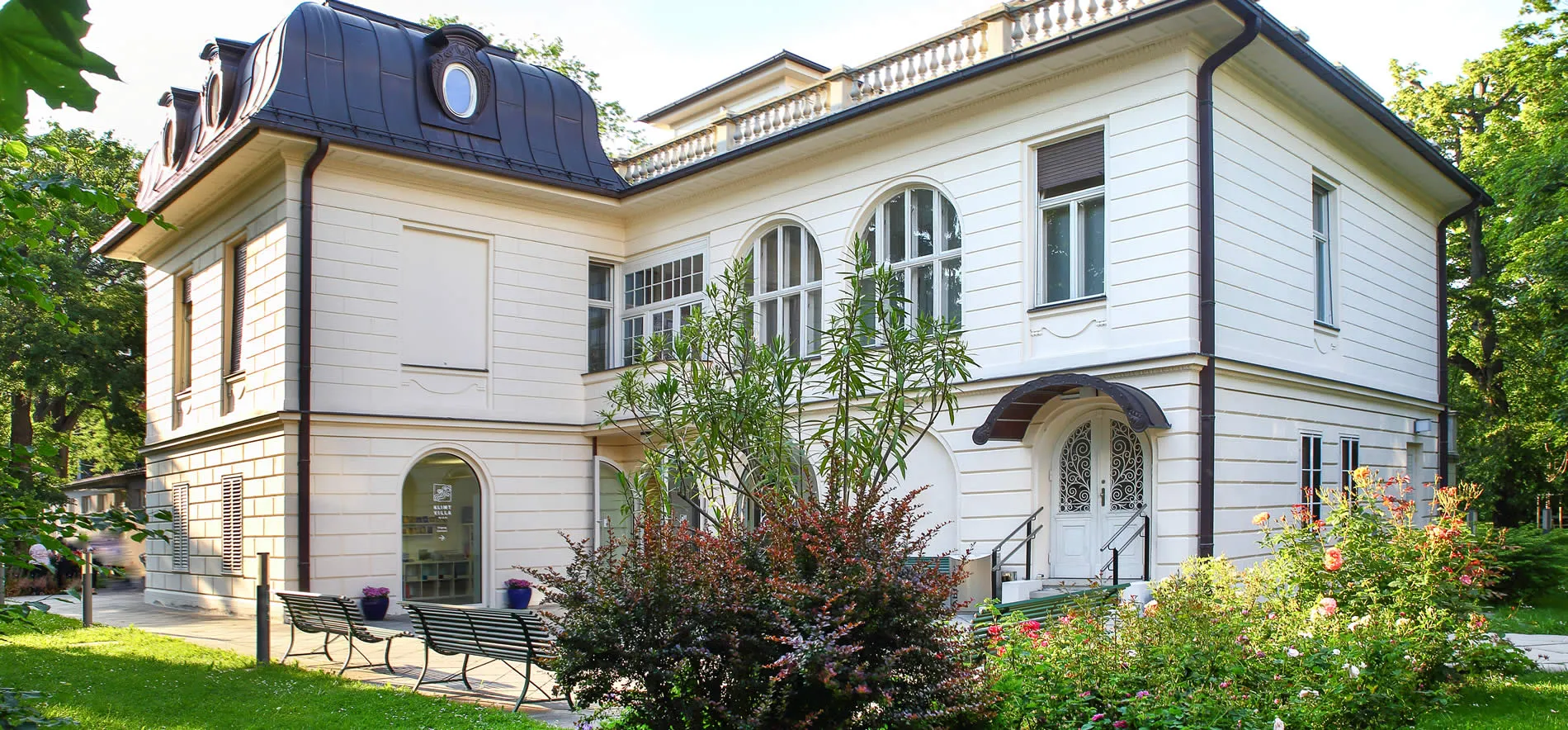 white villa with dark roof and arched windows surrounded by greenery