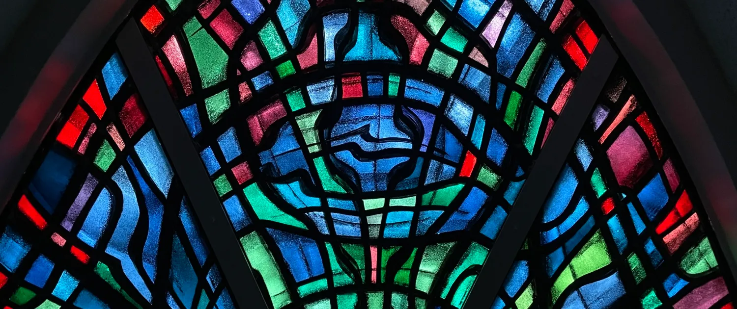 Stained glass window with intersecting arches in vibrant blues, greens, reds, and purples at Kópavogskirkja