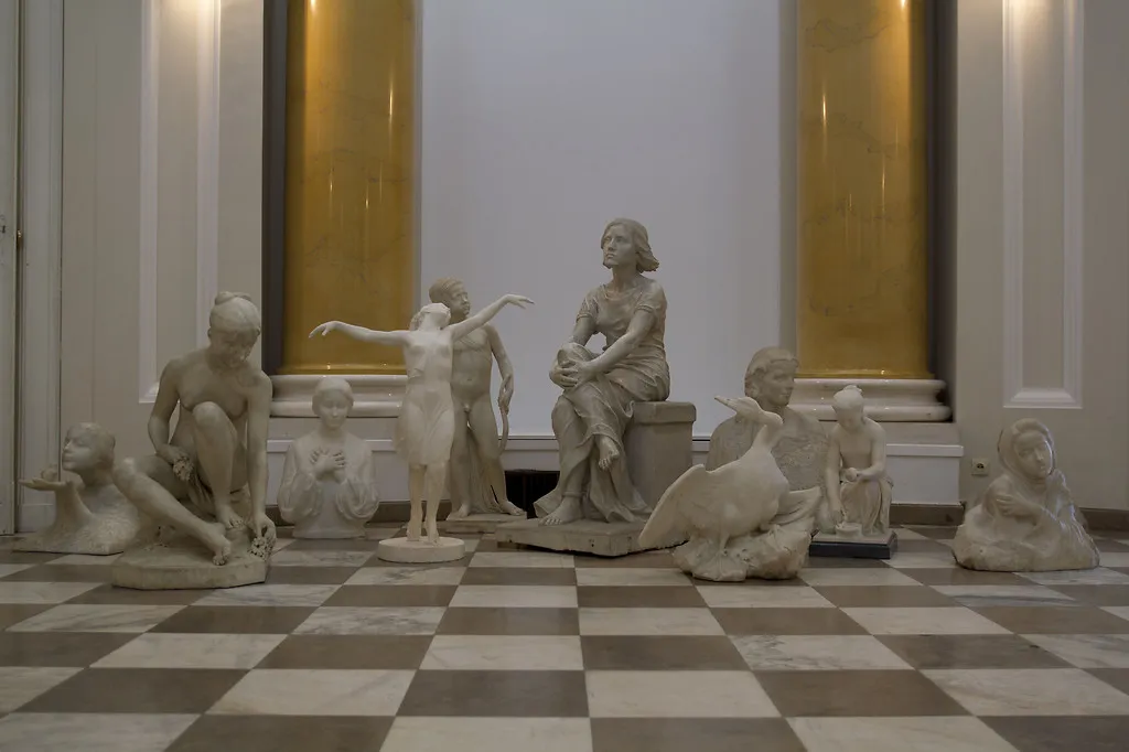 Marmeren sculpturen tentoongesteld in een galerie met een dambordvloer en zuilen