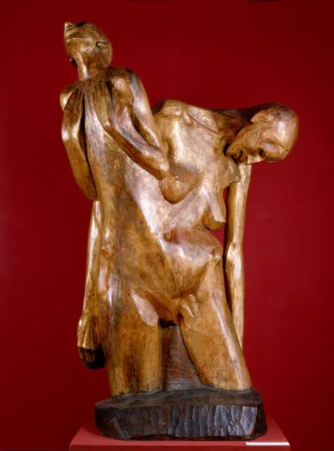 houten beeld van twee omhelzende figuren op rode achtergrond