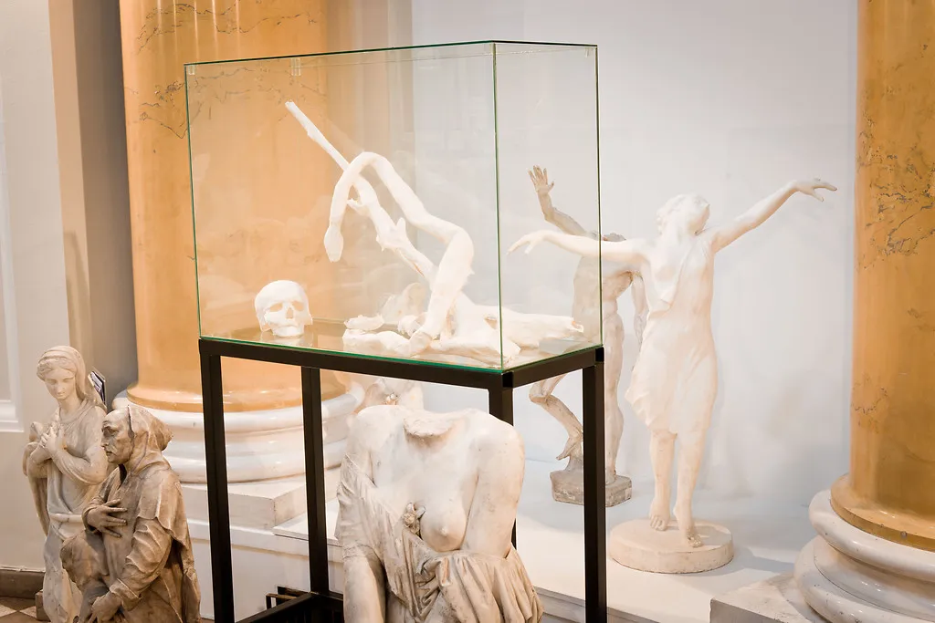 Witte marmeren sculpturen tentoongesteld in een glazen vitrine en op sokkels in een galerij met zuilen