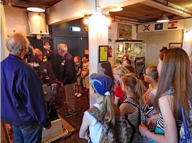 Grupo de visitantes escuchando a un guía en un taller industrial con maquinaria y vitrinas