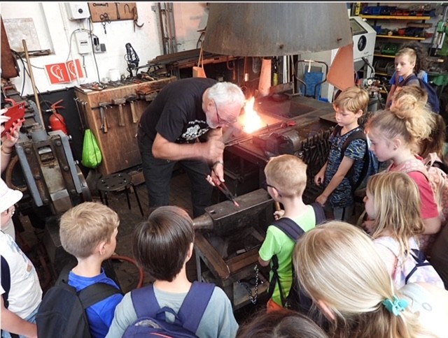 Grupo de niños observando una demostración de metalurgia con una fragua incandescente en un taller