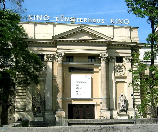 The Künstlerhaus Wien building with a classical facade, columns, statues, and a sign that reads 'KINO KÜNSTLERHAUS KINO' under a blue sky.