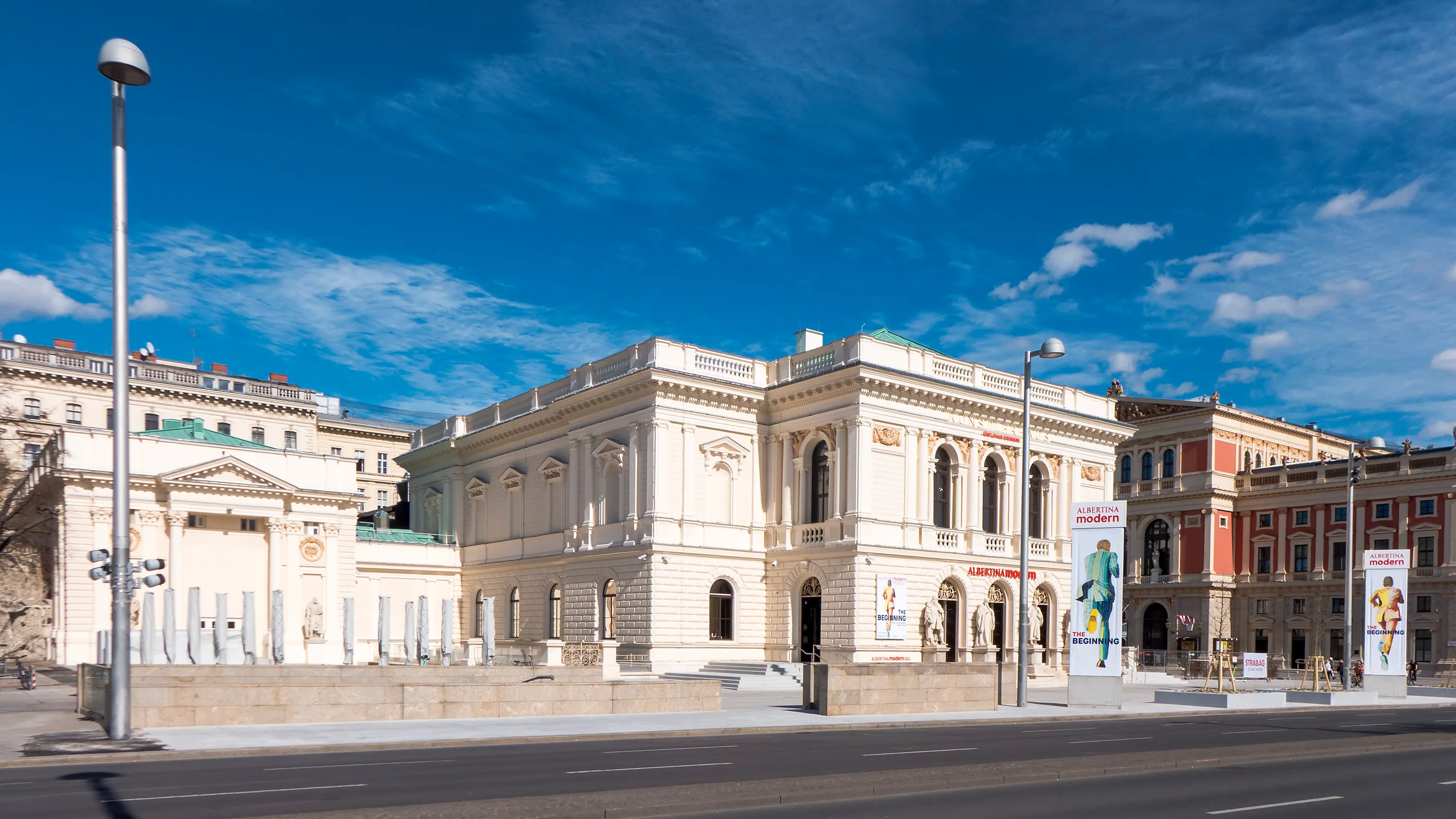 Wit klassiek gebouw met boogramen en zuilen aan de Karlsplatz onder een blauwe hemel