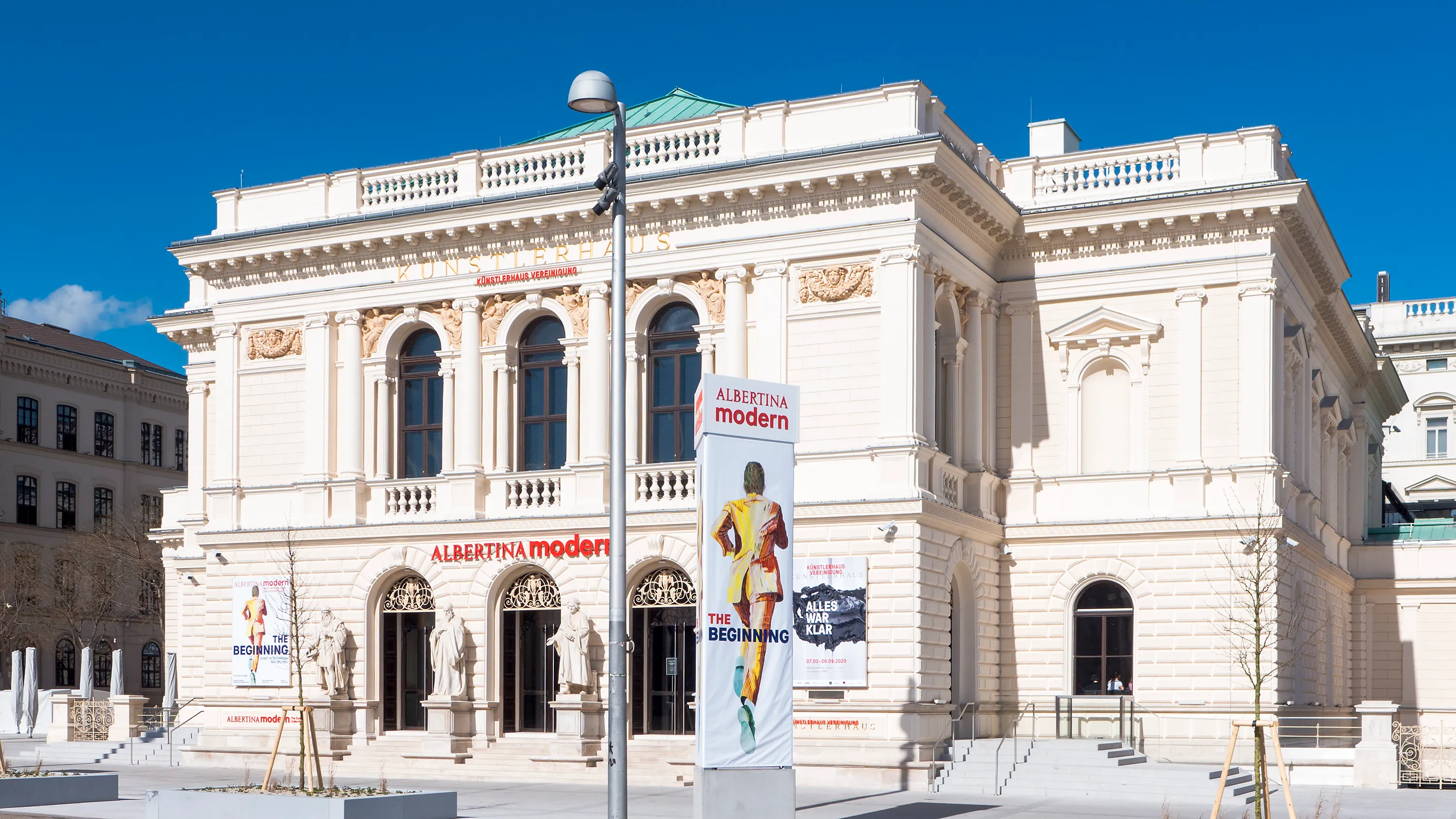 Klassiek gebouw met boogramen en sierlijke details, met een 'Albertina modern'-banner op de gevel onder een blauwe hemel