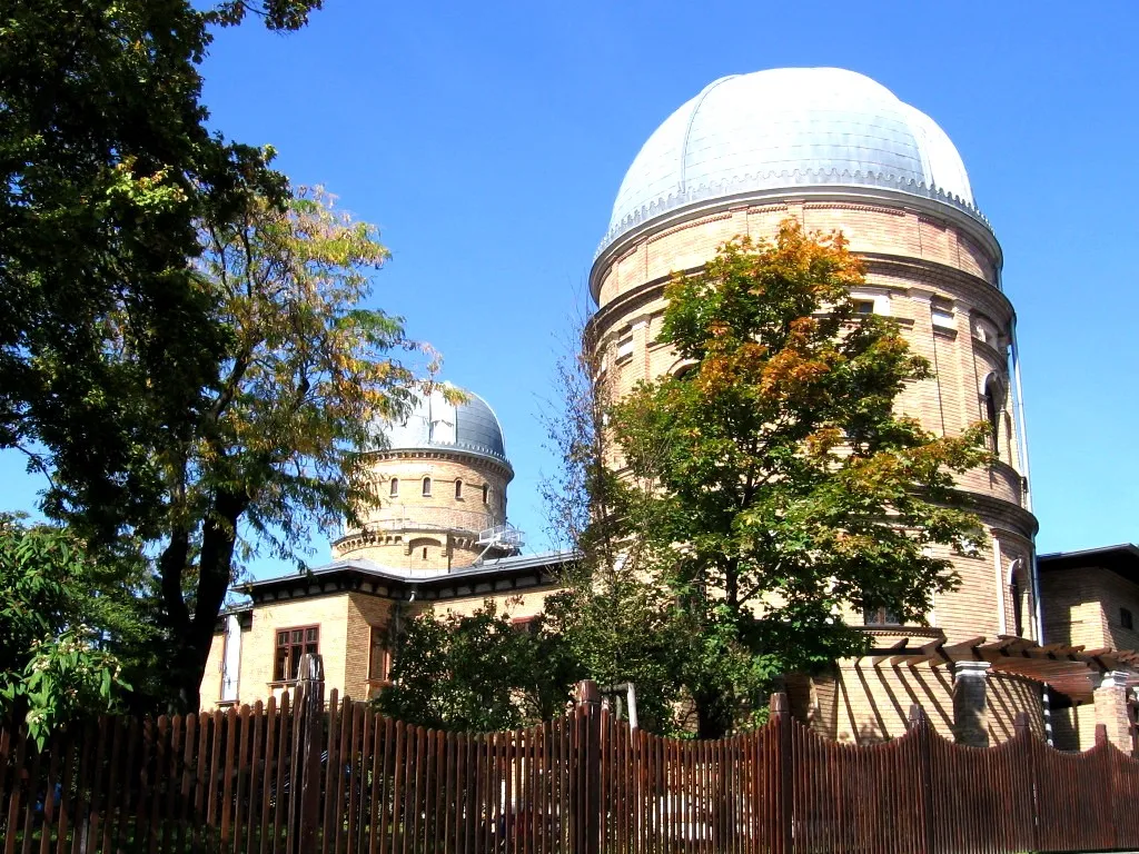 El Observatorio Kuffner con dos grandes edificios abovedados, uno más grande que el otro, contra un cielo azul con árboles en primer plano.