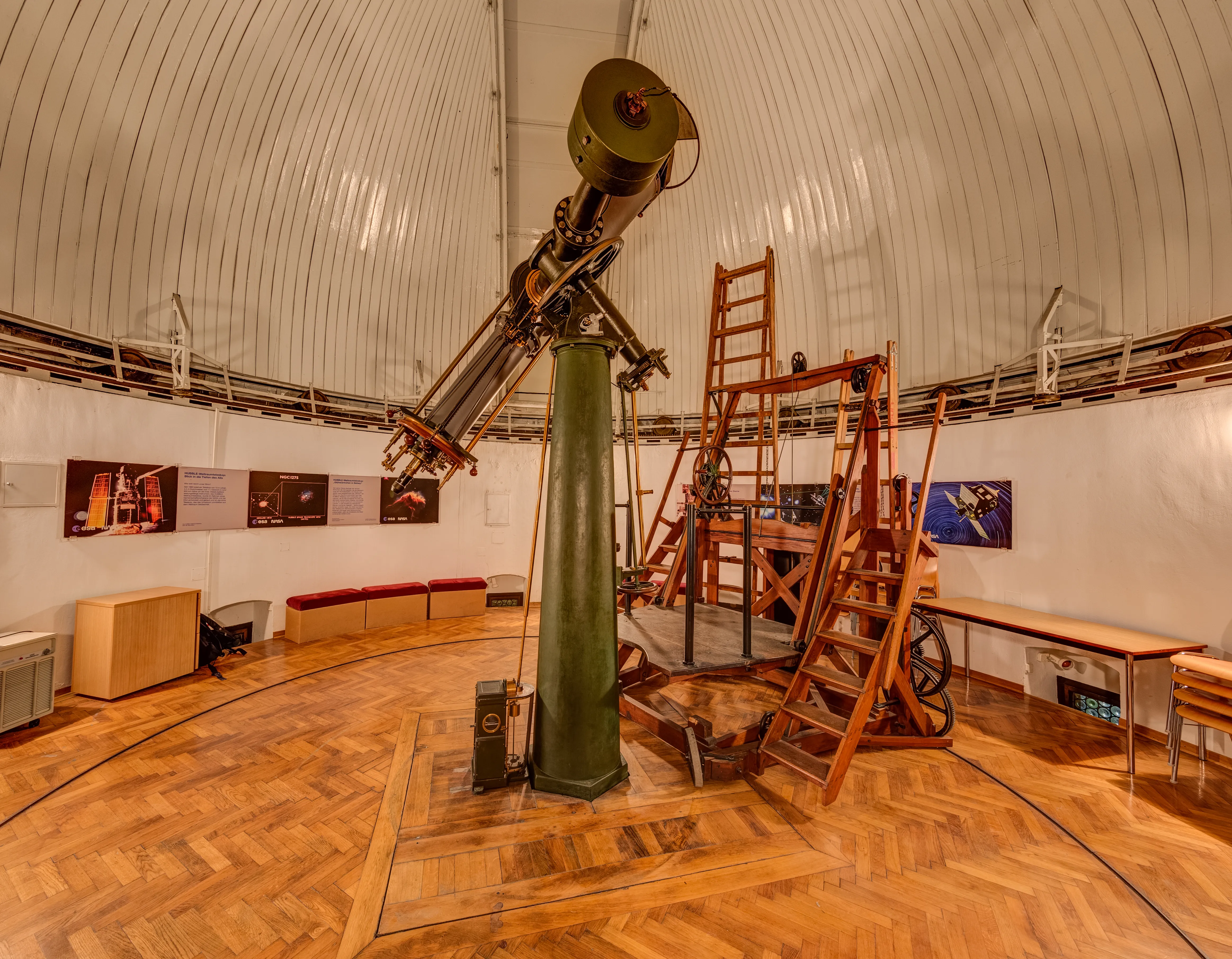Interior del Observatorio Kuffner con un gran telescopio sobre un pedestal verde, una escalera de madera y un techo abovedado