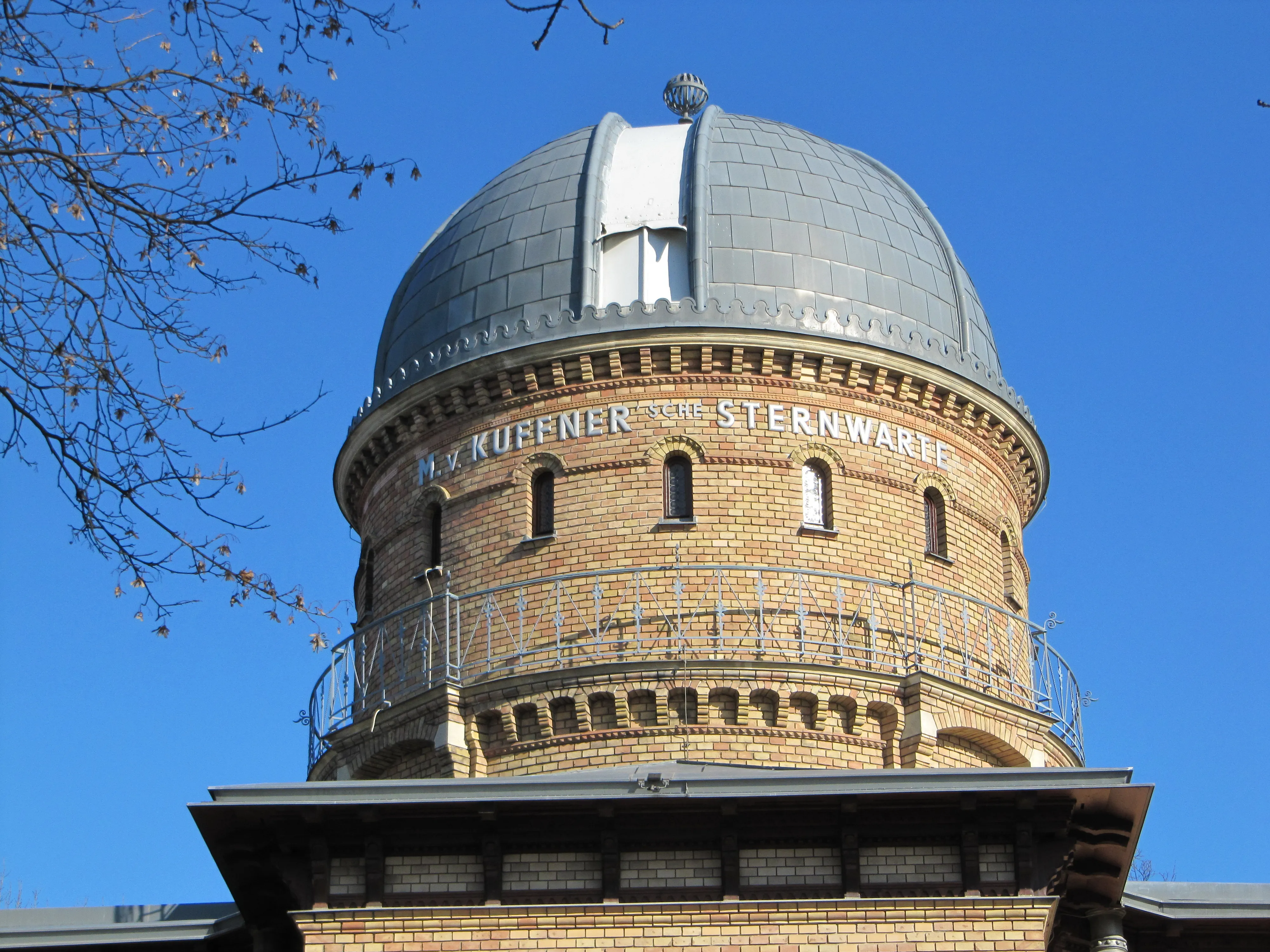 Torre observatorio de ladrillo con una gran cúpula e inscripción 'KUFFNER STERNWART' bajo un cielo azul claro