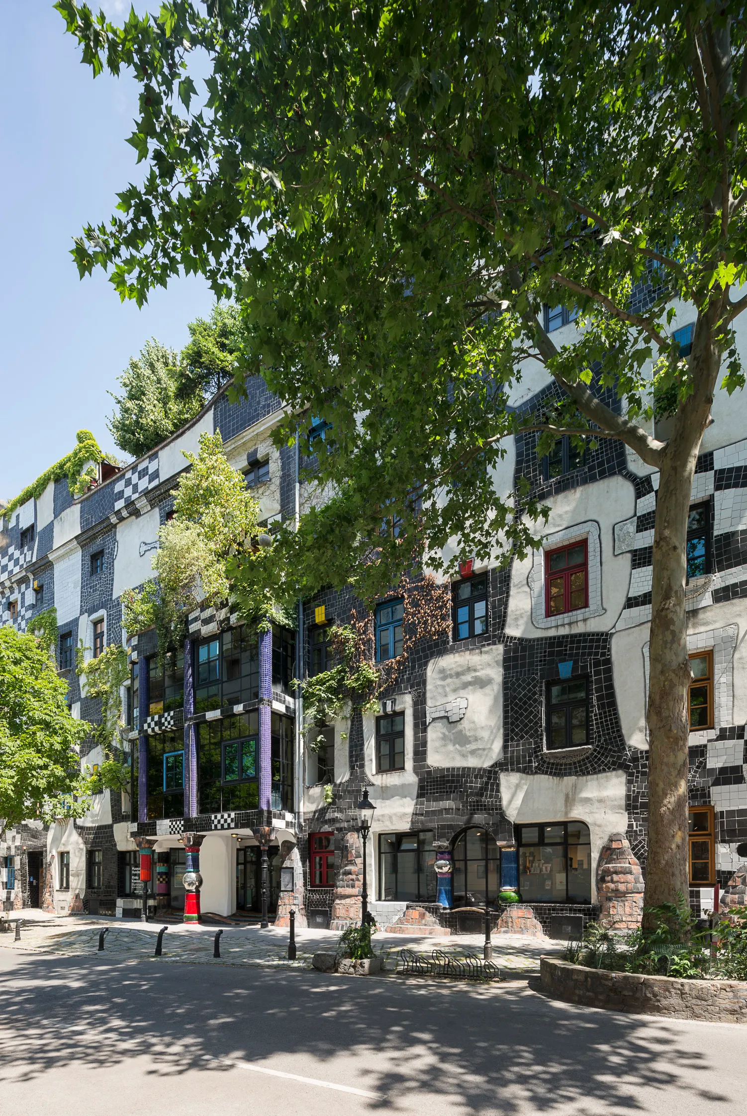 Zewnątrz Kunst Haus Wien z kolorową fasadą z mozaiki, nieregularnymi oknami i drzewami z przodu