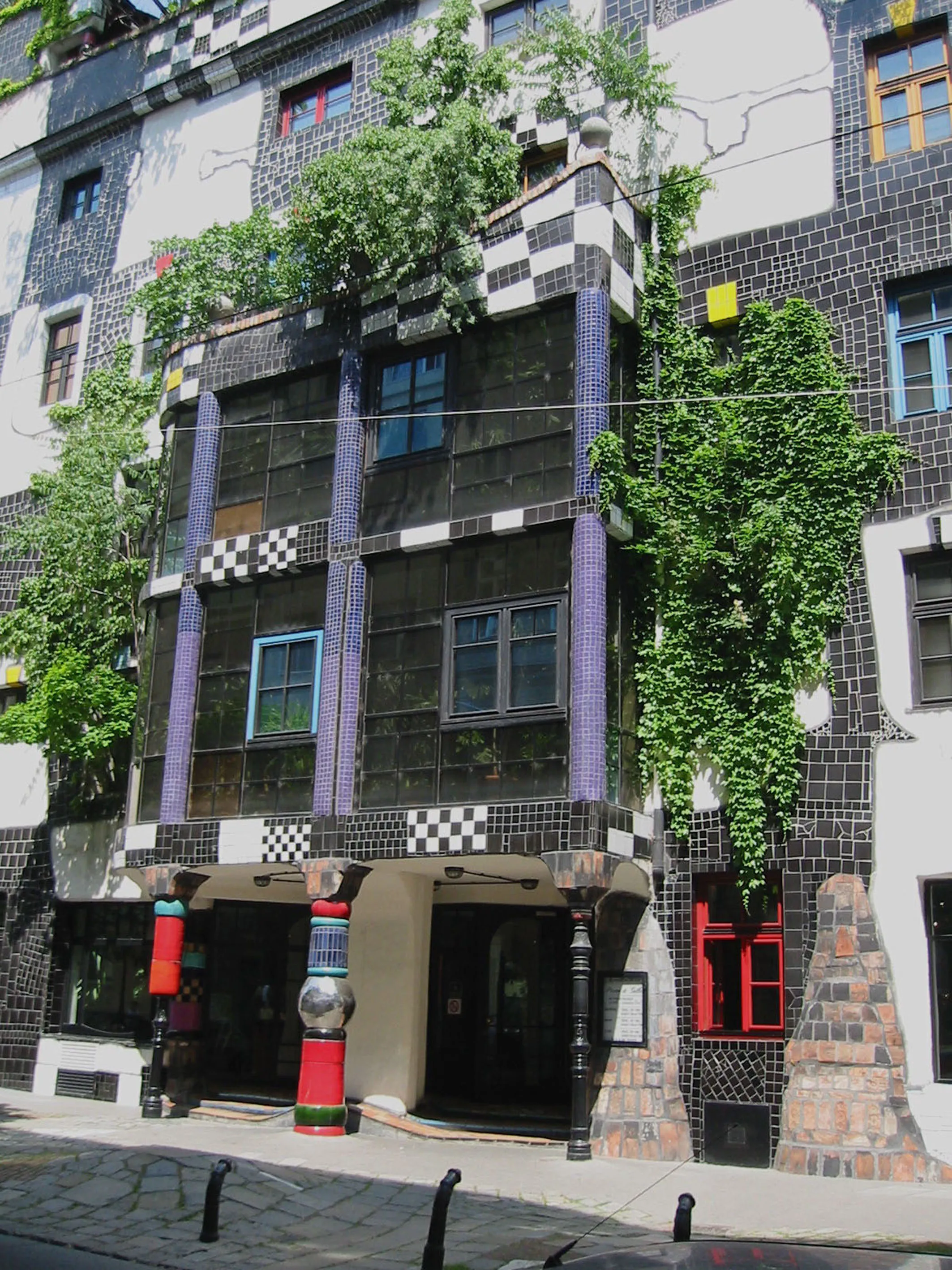 Kolorowa i unikalna fasada Kunst Haus Wien z mozaikowymi płytkami, zielonymi roślinami rosnącymi na ścianach i nieregularnymi oknami.