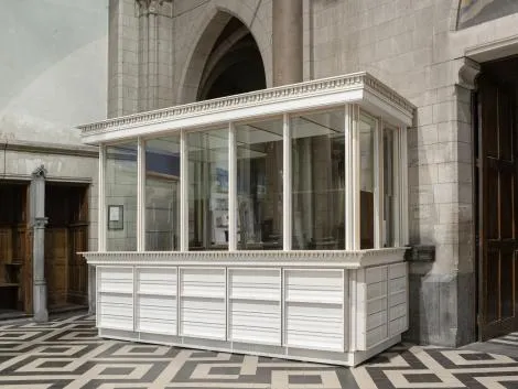 Quiosco blanco con paredes de cristal dentro de un edificio histórico con un patrón geométrico de suelo en blanco y negro y puertas de piedra arqueadas