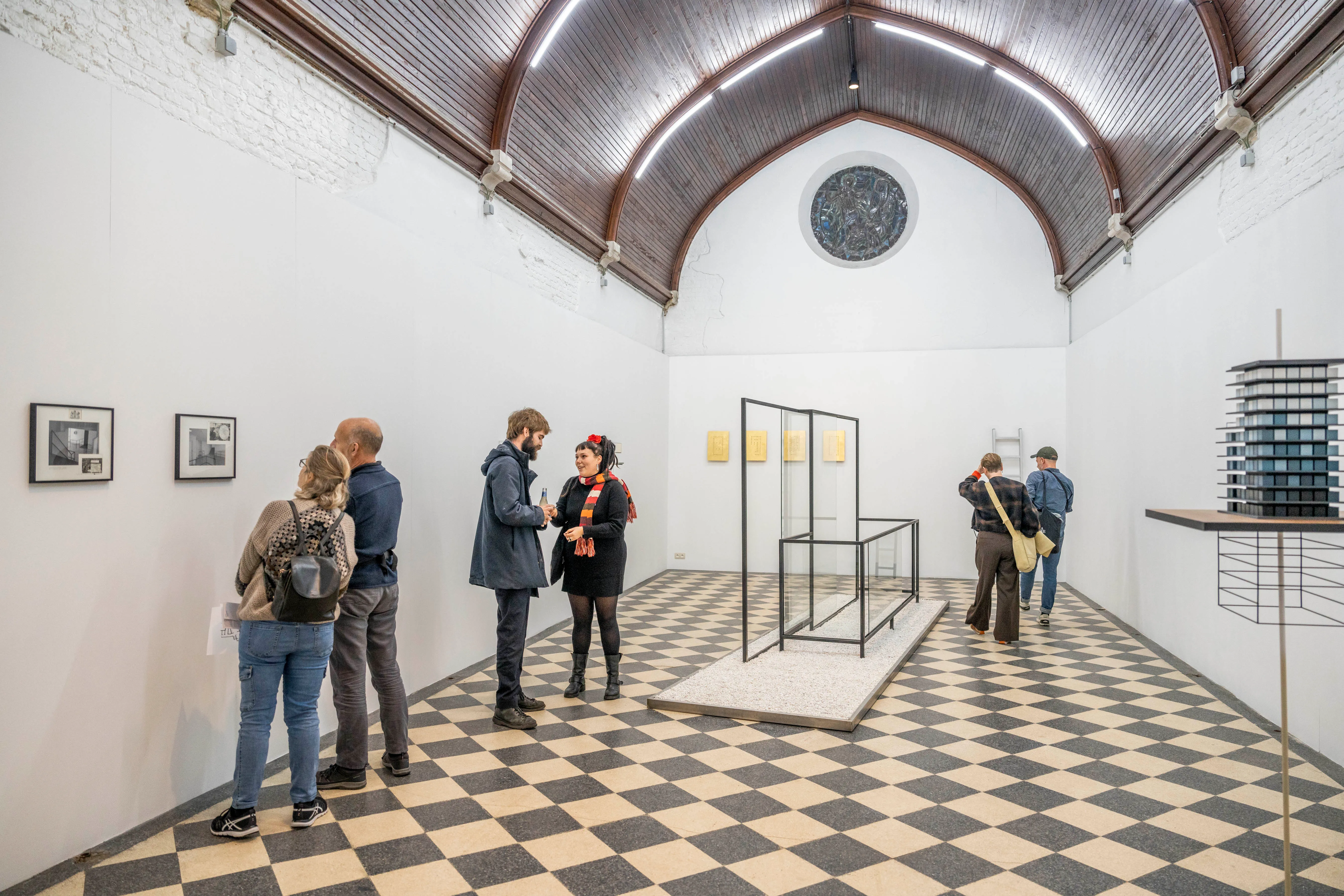 Interior de Kunsthal Extra City que muestra un gran vestíbulo con un techo abovedado, suelo de damero en blanco y negro, un rosetón y visitantes observando obras de arte enmarcadas y exposiciones