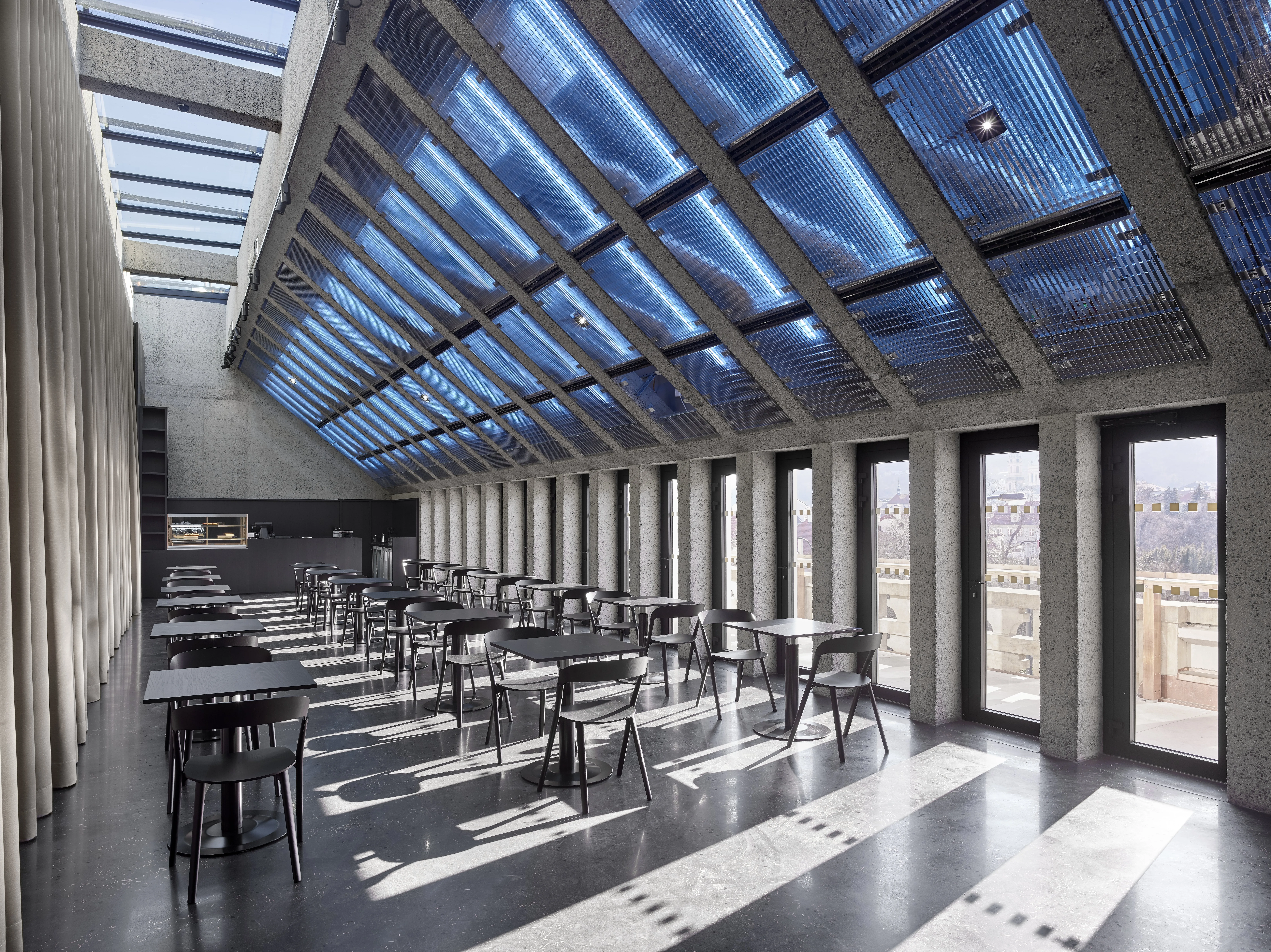 Interior of Kunsthalle Praha with a blue glass ceiling, rows of tables and chairs, and large windows