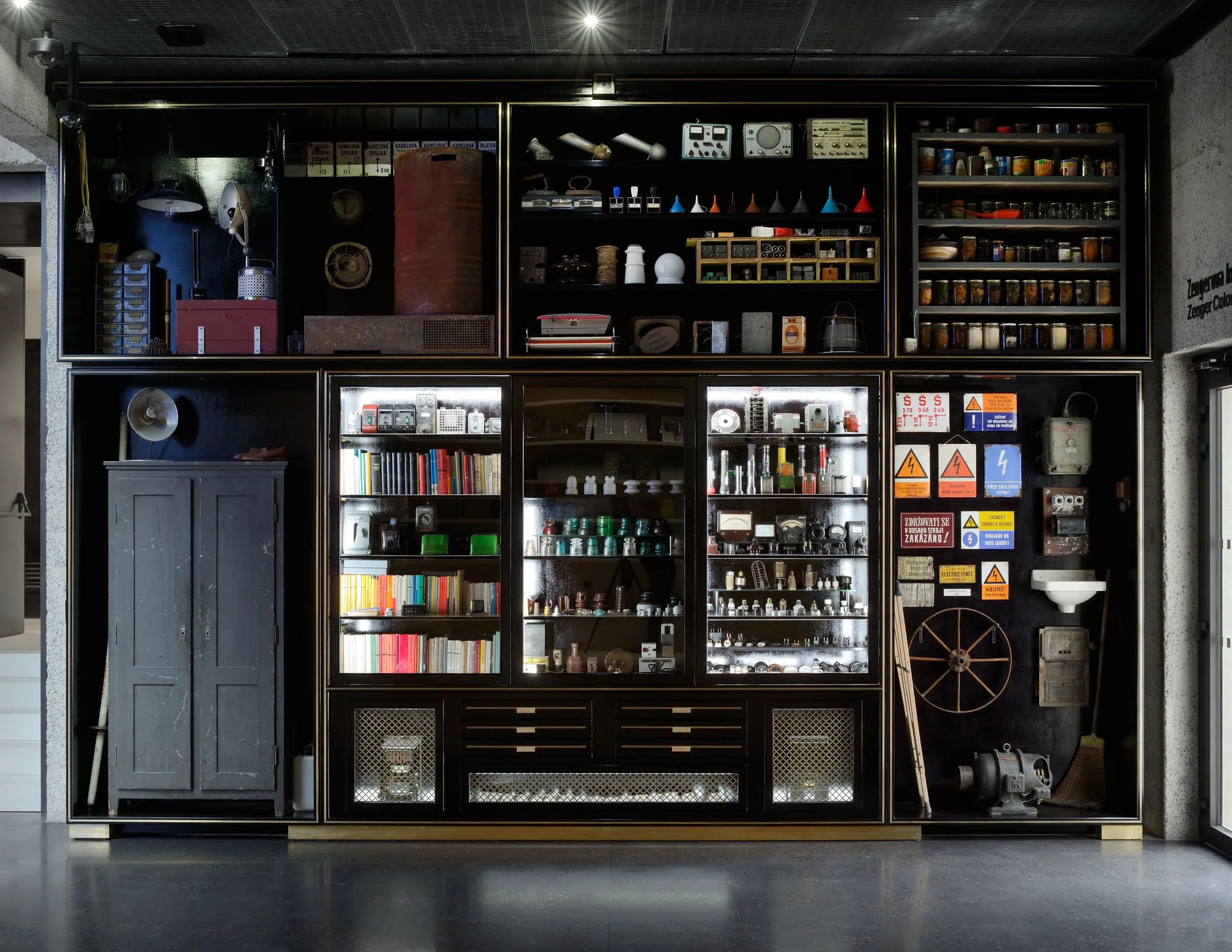 Interior display cabinet with shelves holding books, bottles, and various objects in a dark room