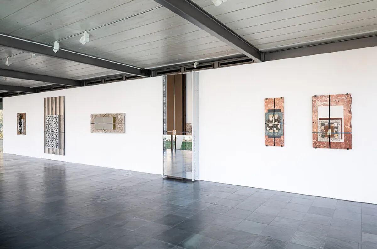 Gallery space with artworks on white walls, dark floor, and exposed ceiling beams