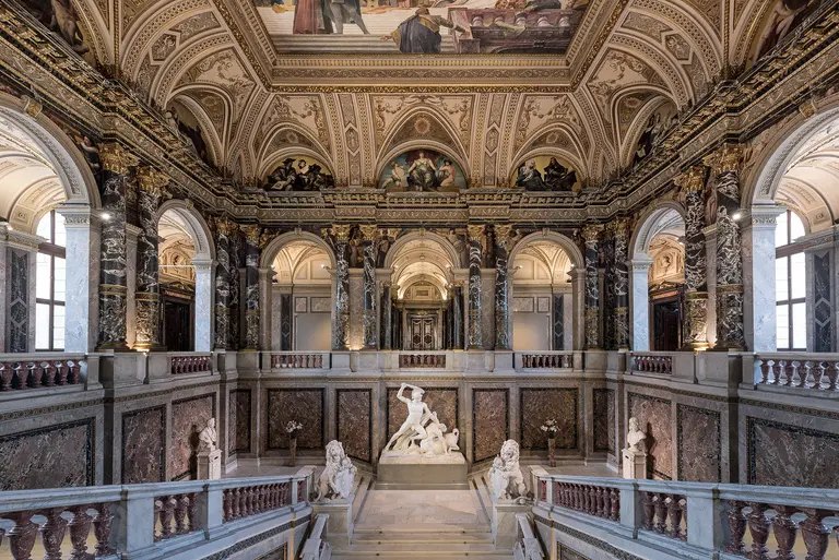 Salón interior ornamentado con techos abovedados, escaleras de mármol y esculturas clásicas en un gran museo.