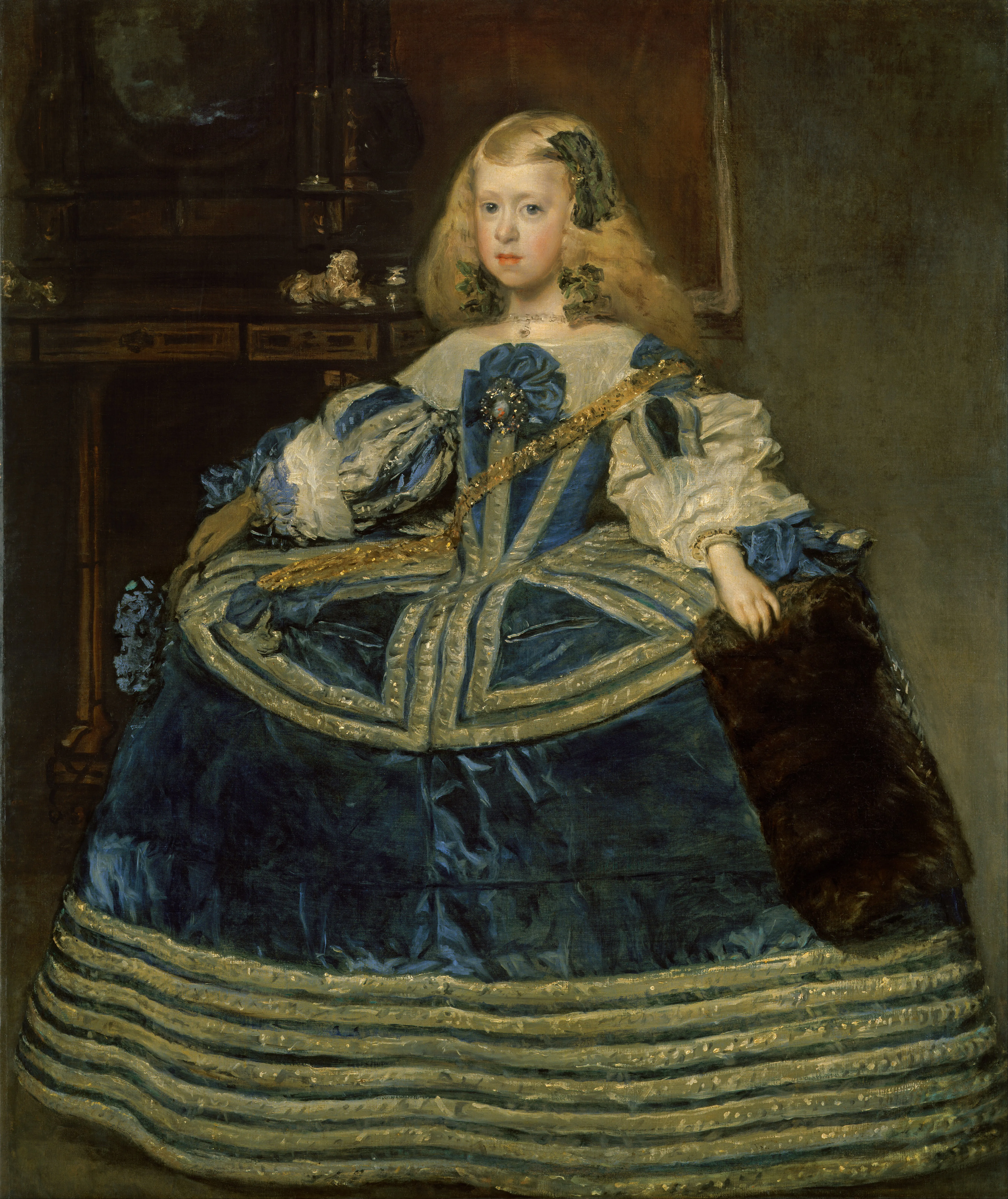 Una mujer con un vestido ornamentado en azul y blanco con ribete dorado y una estola de piel, sentada frente a un fondo oscuro con un armario de madera.