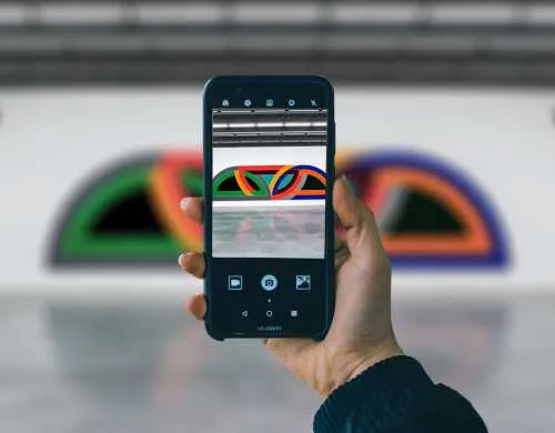 Mano sosteniendo un teléfono inteligente fotografiando una colorida obra de arte contemporánea en forma de arco en la galería de un museo