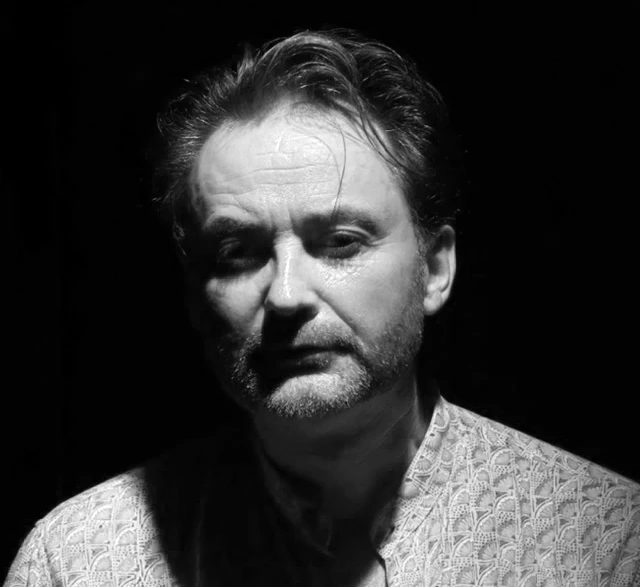 portret mężczyzny w stylu czarno-białym z brodą i wzorzystą koszulą na ciemnym tle