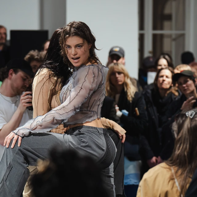 Two performers in a close embrace during a live art performance, with an audience watching in the background.