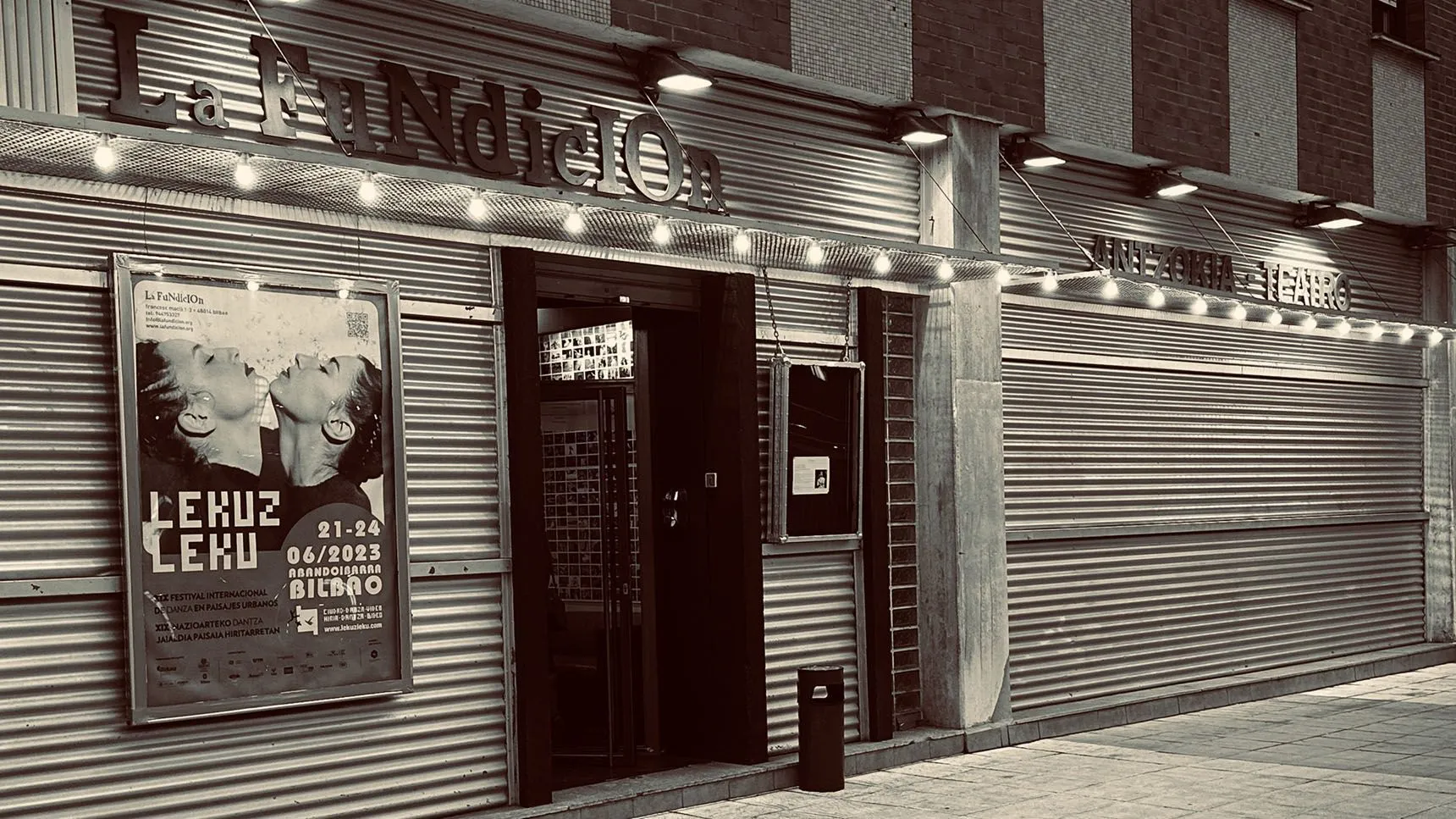 Fasada zewnętrzna La Fundición Bilbao ze ścianami z blachy falistej, podświetlanym szyldem i plakatem teatralnym
