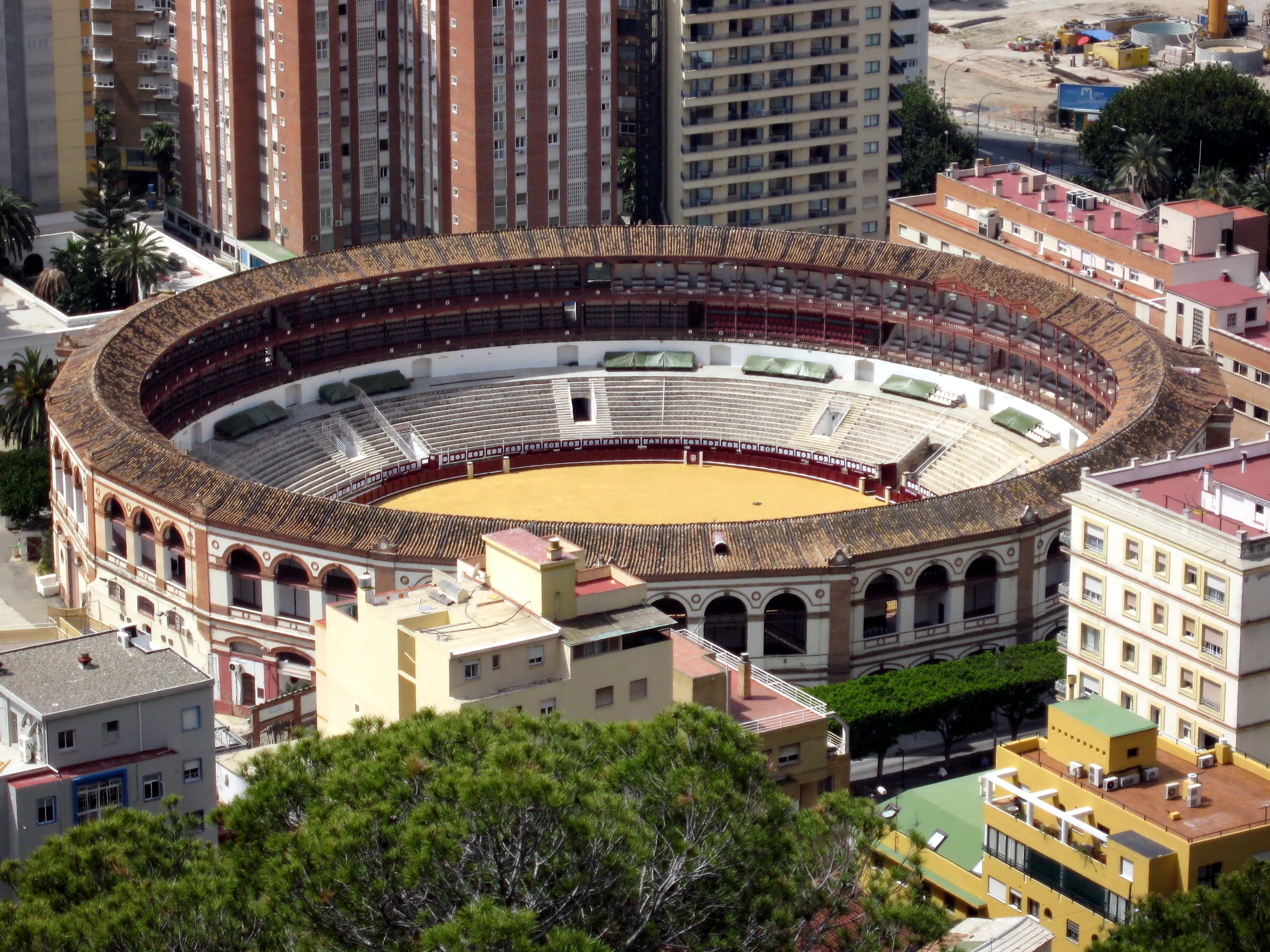Vista aérea de la plaza de toros circular Plaza de Toros de La Malagueta con su arena, tendidos y fachada de arcos, rodeada de edificios residenciales en Málaga.