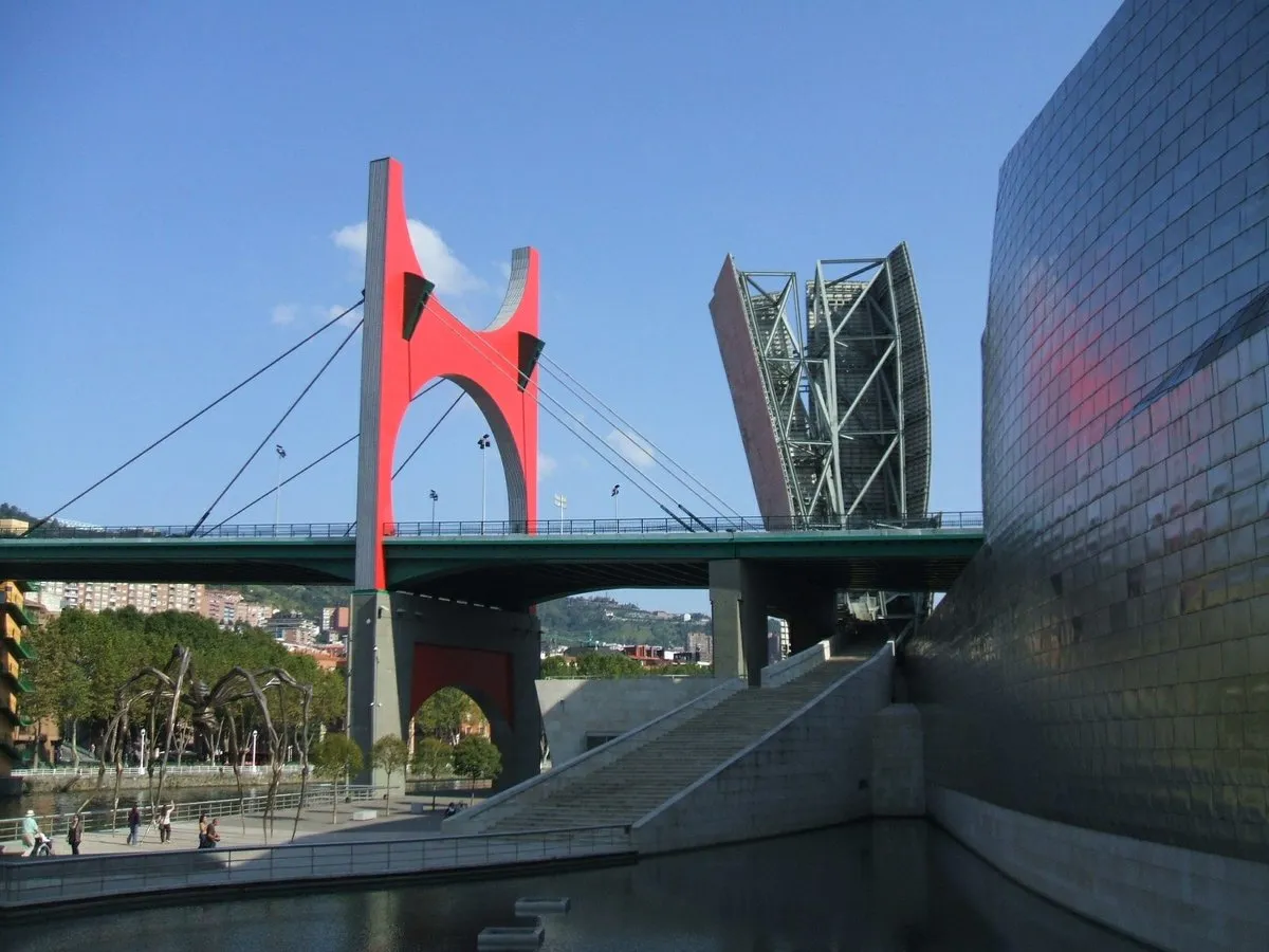 De La Salve-brug met de rode L'Arc Rouge-boog van Daniel Buren naast het met titanium beklede Guggenheim Museum Bilbao onder een strakblauwe lucht