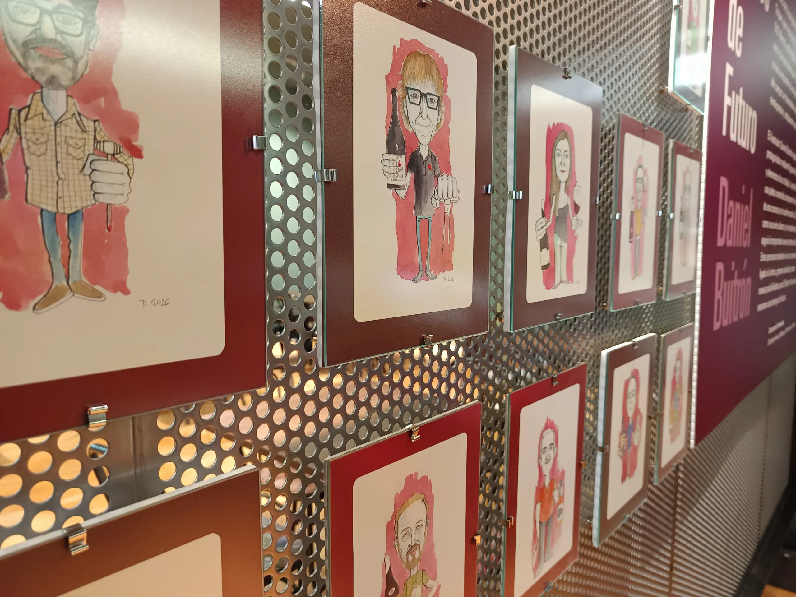 Retratos caricaturizados enmarcados expuestos sobre una pared de metal perforado en una sala de exposiciones