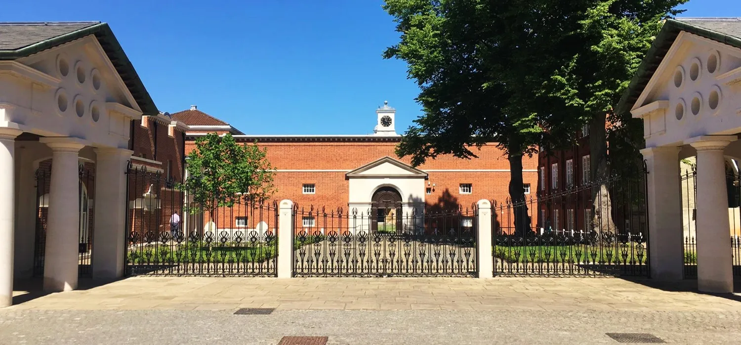 Szeroki widok na Leatare Quadrangle w Lady Margaret Hall, przedstawiający budynki z czerwonej cegły otoczone białymi klasycznymi portykami z żelaznymi balustradami pod bezchmurnym niebem.