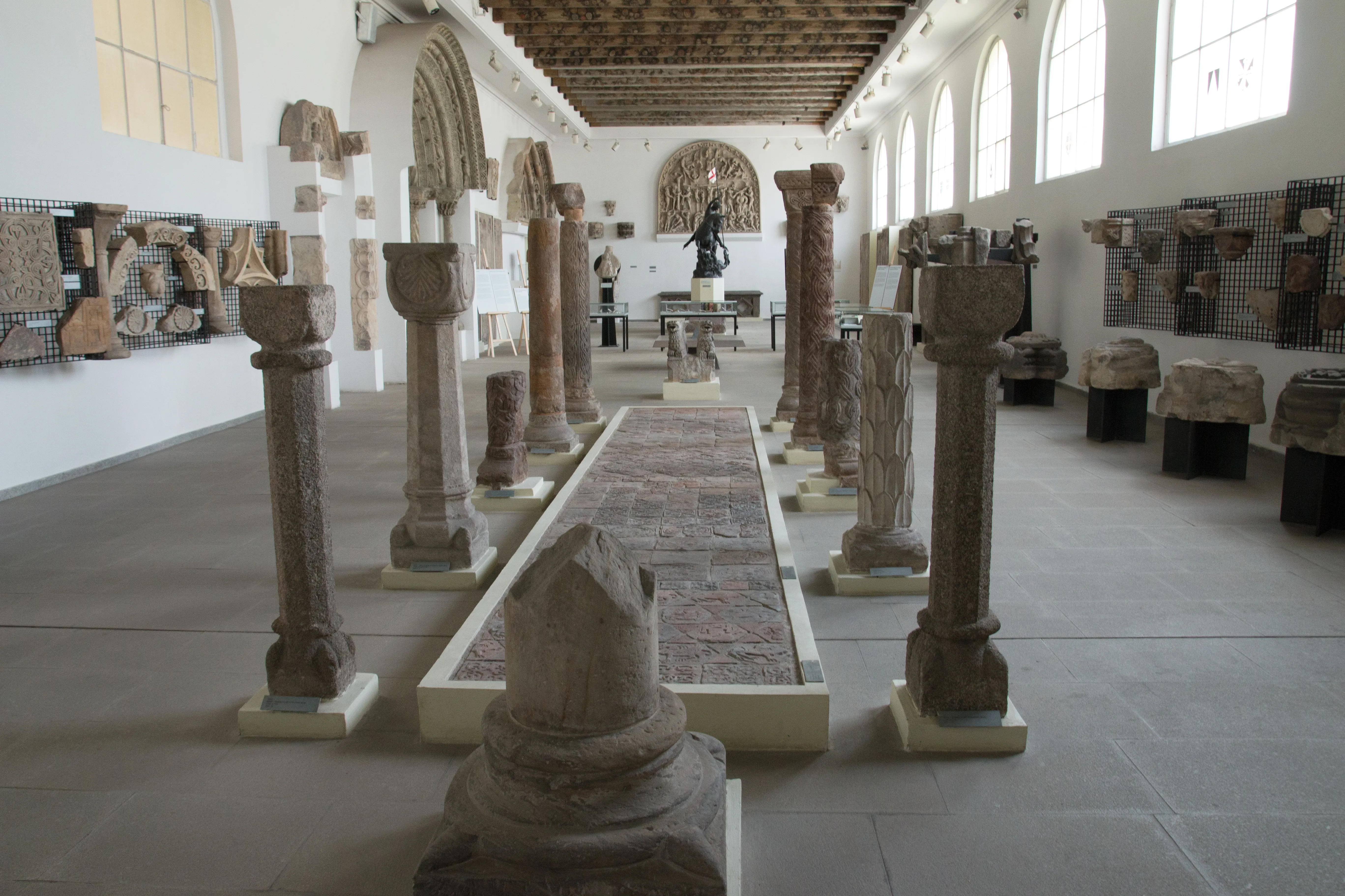 Interieur van een museumgalerij met stenen zuilen en architectonische fragmenten tentoongesteld op sokkels en muren