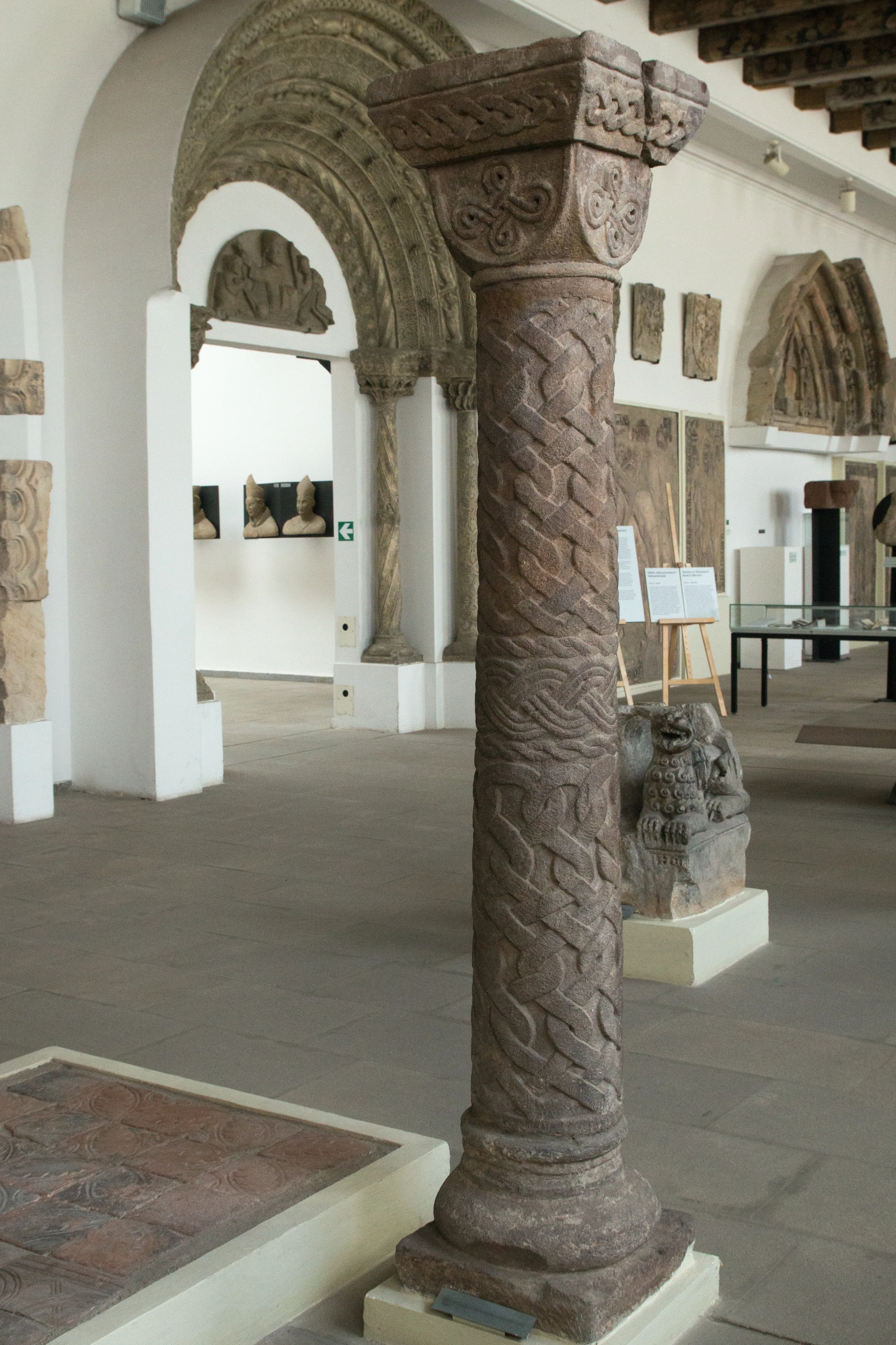 een ingewikkeld gesneden stenen zuil in een museumgalerij met andere sculpturen op de achtergrond