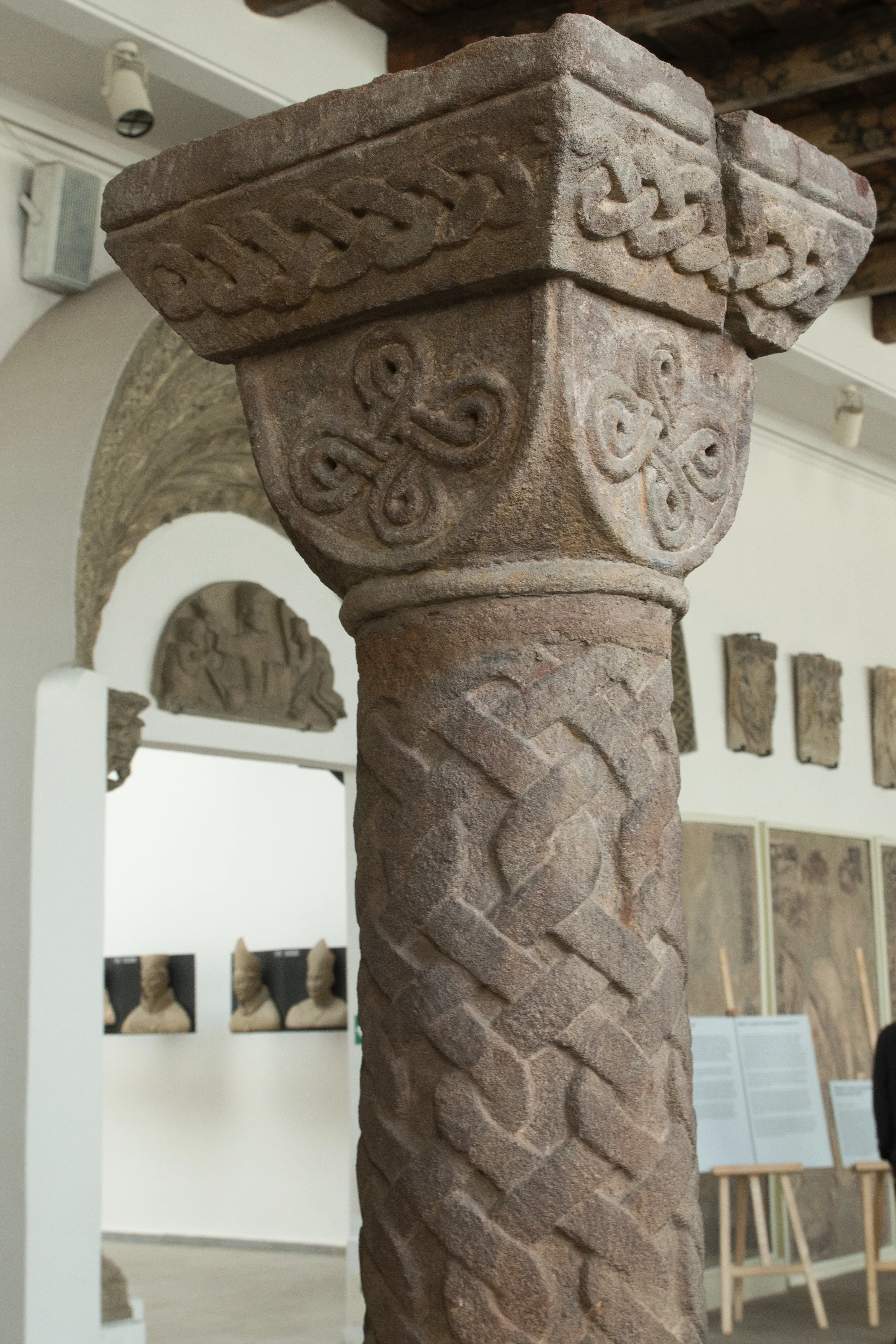 Close-up van een bewerkte stenen zuil met Keltische knopen en een gedraaide touwversiering in een museumgalerij