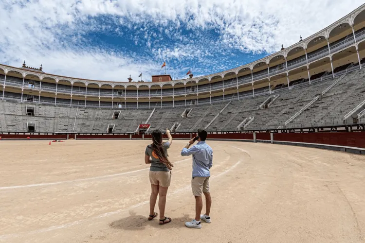 Twee mensen die staan in de zanderige arena van de Plaza de Toros de las Ventas, met de gebogen zitplaatsen en bogen van de arena zichtbaar op de achtergrond.