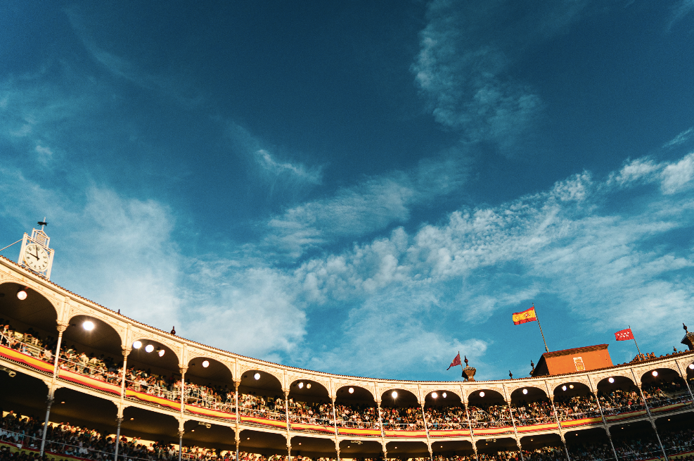 Circular bullring with arched seating under a blue sky with white clouds