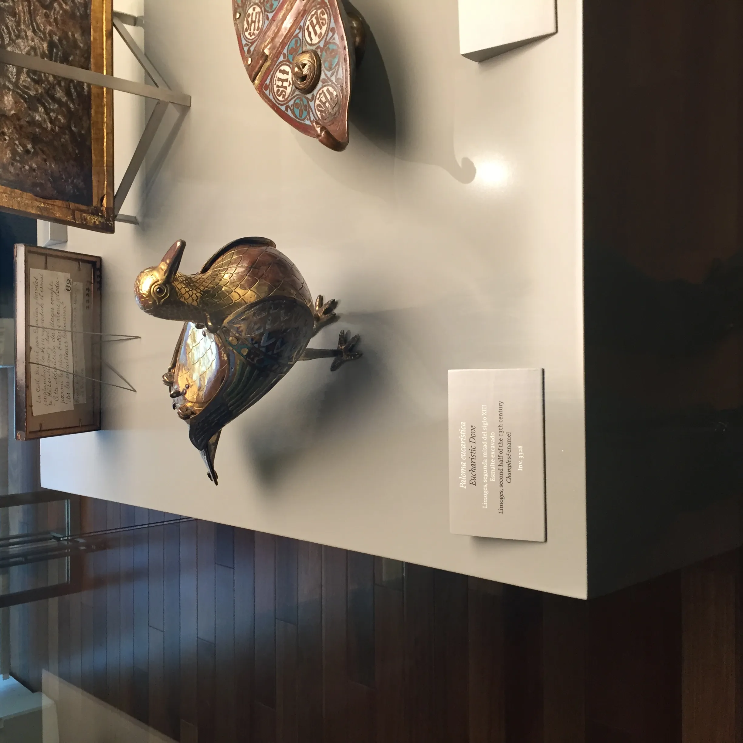 Artefacto dorado en forma de pato sobre una mesa de exhibición blanca en una galería de museo
