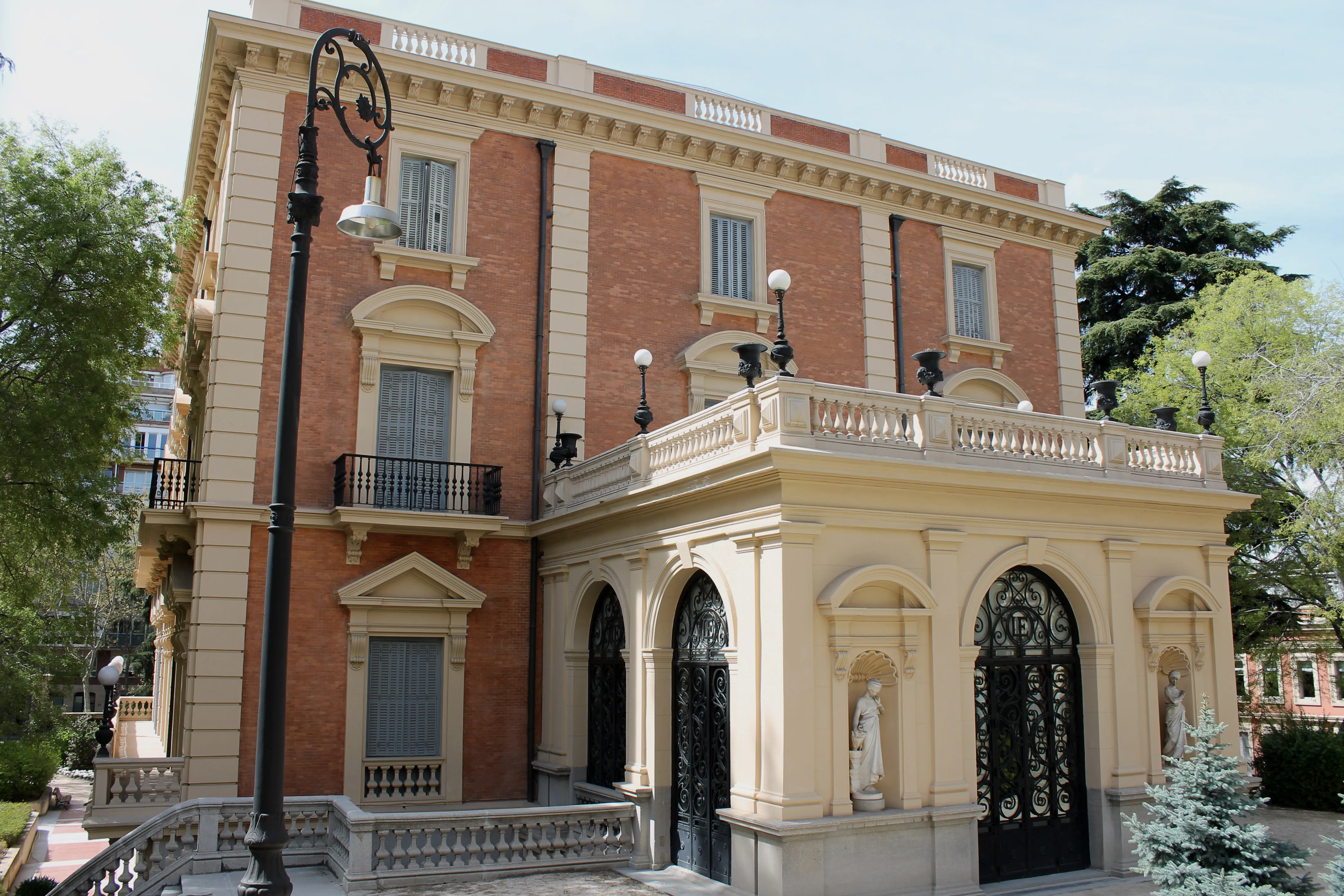 Mansión neorrenacentista con ladrillo rojo y estuco crema, entradas arqueadas, balcones y una farola decorativa en el frente