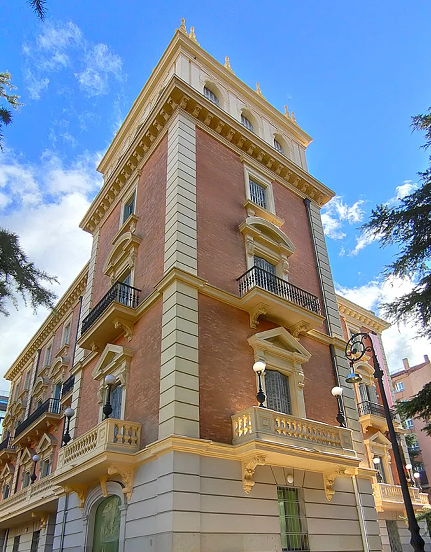 Edificio neorrenacentista con fachada amarilla y terracota, balcones ornamentados y detalles arquitectónicos clásicos bajo un cielo azul