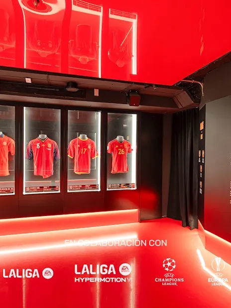 Red-lit exhibition hall with football jerseys in glass cases and LaLiga and UEFA Champions League logos on the floor