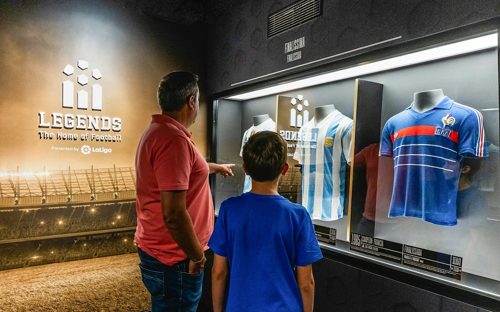 A man and a boy looking at football jerseys in a glass display case at Legends: The Home of Football.