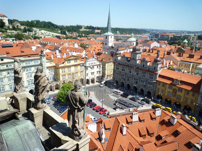 View from a tower overlooking red-roofed buildings and a city square with a church spire in the distance