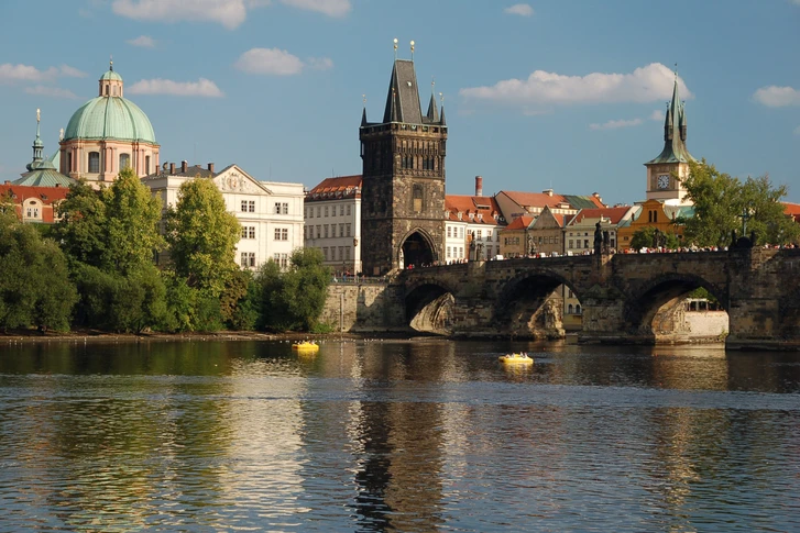 The Lesser Town Bridge Tower on Charles Bridge with a river in the foreground and historic buildings in the background