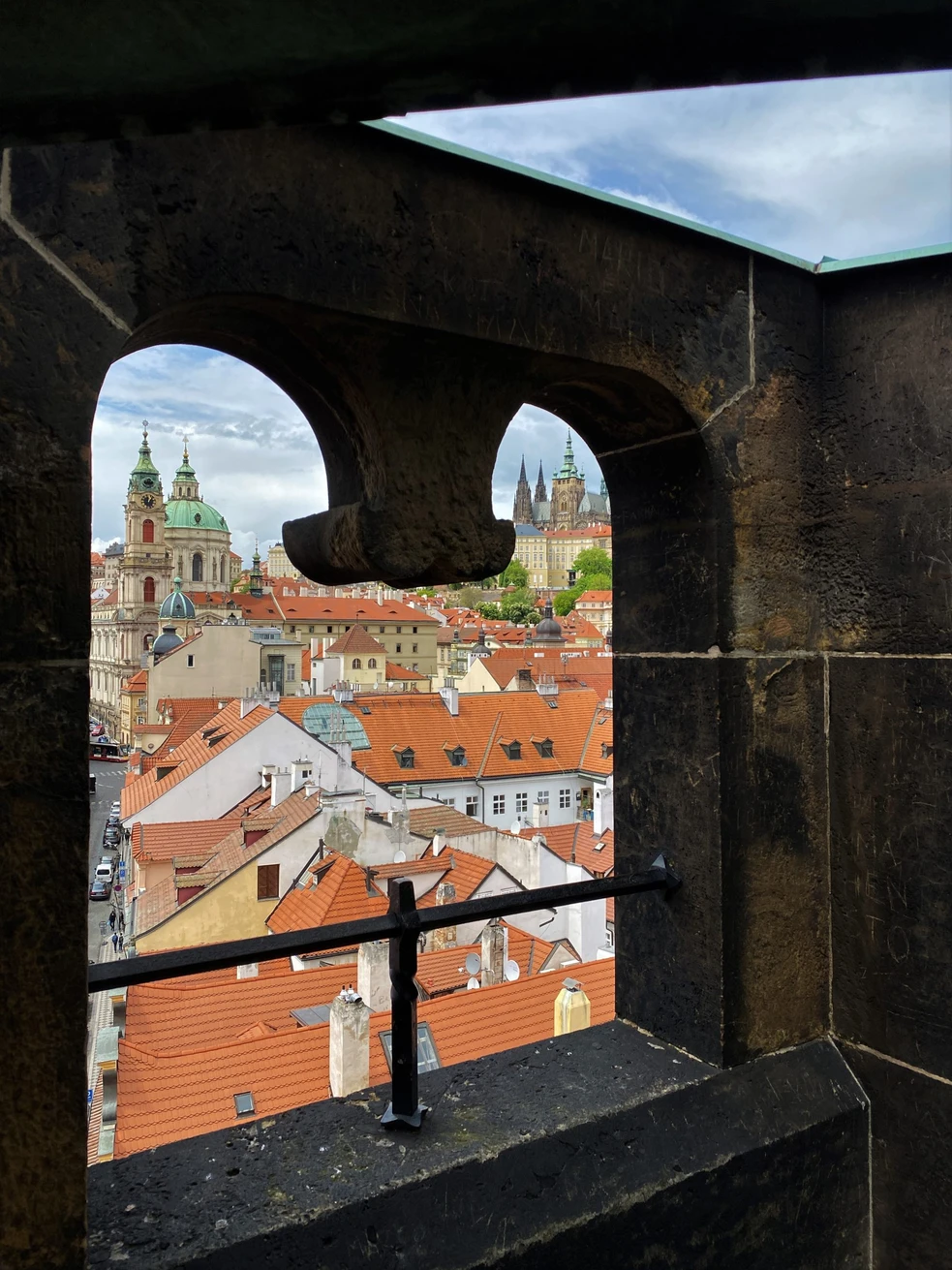 Vista desde una ventana de piedra que da a edificios de tejados rojos y campanarios de iglesias en Praga
